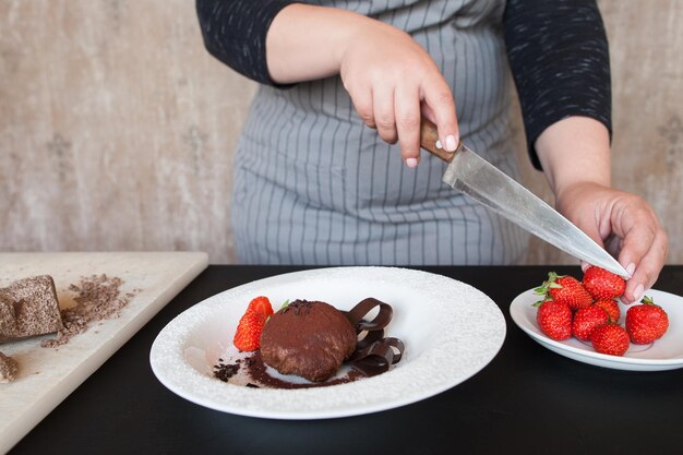 Mujer cocinera decora un delicioso postre de chocolate con fresa Proceso de hacer arte culinario de fondant con frutos rojos frescos