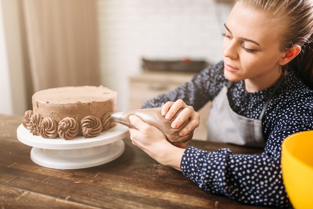 Mujer cocinera decorar pastel de chocolate con jeringa culinaria.