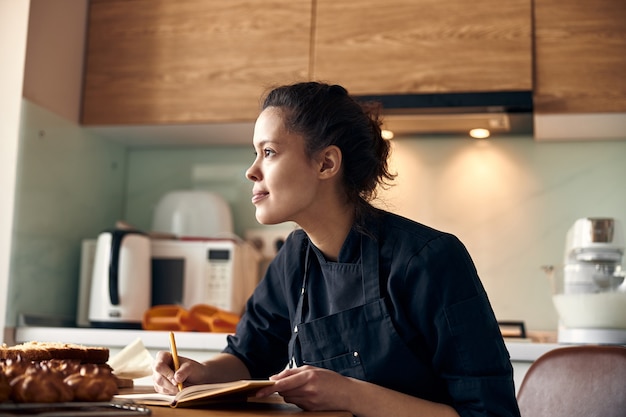 Foto mujer cocinera profesional está escribiendo una receta de canutillos en la cocina ligera moderna