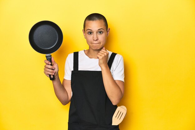 Foto mujer cocinera con una sartén de fondo de estudio amarillo confundida se siente dudosa e insegura