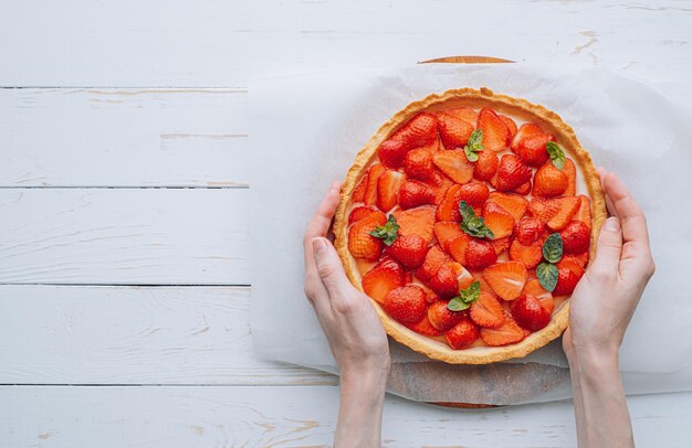 Mujer cocinera sosteniendo un pastel con crema pastelera de fresas y menta