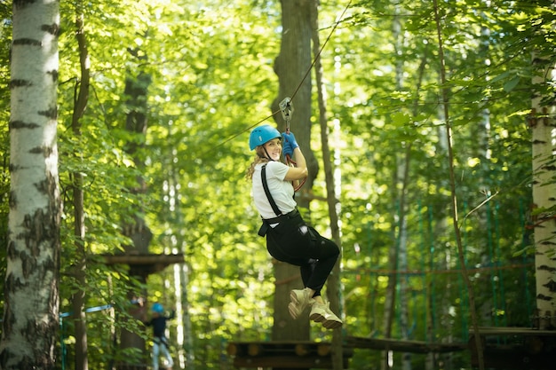 Una mujer colgada del cable de seguro de su cinturón en la atracción de entretenimiento del puente de cuerda del bosque