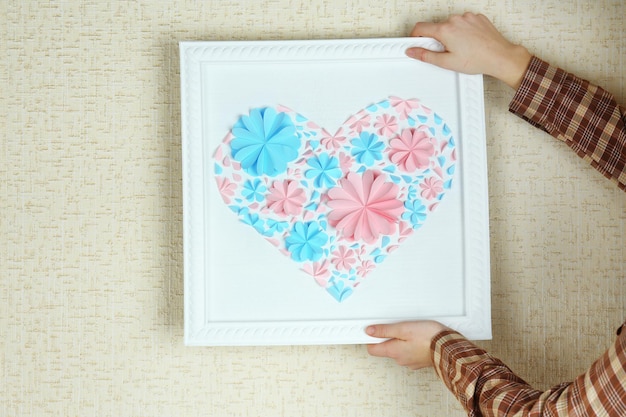 Mujer colgando un cuadro con corazón de flores de papel