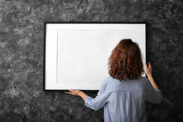 Mujer colgando marco de fotos en blanco en la pared oscura