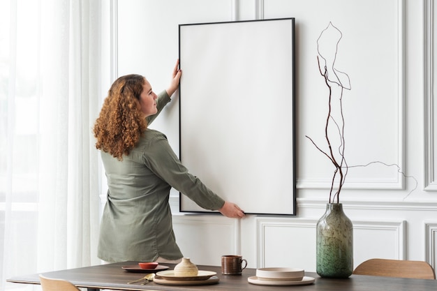 Mujer colgando marco de imagen en blanco en la pared