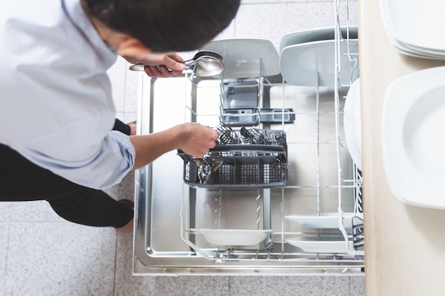 Mujer colocando los cubiertos en el lavavajillas en la cocina de su departamento