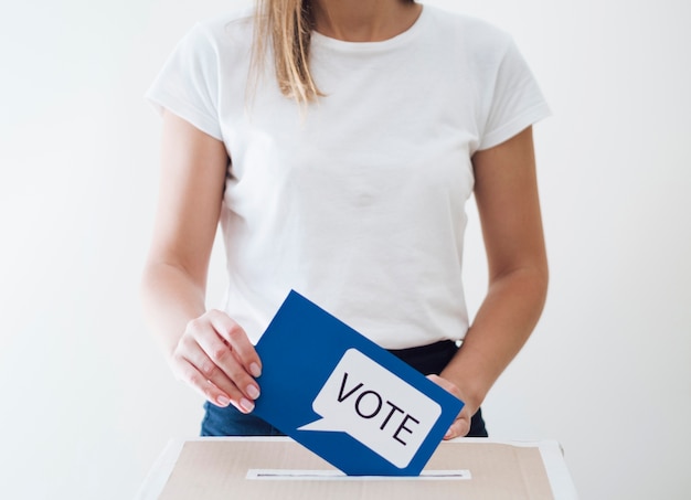 Foto mujer colocando tarjeta azul con mensaje de votación en un cuadro