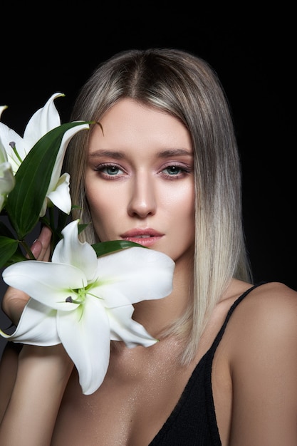 Mujer de color de cabello rubio con flor de lirio sobre fondo negro.