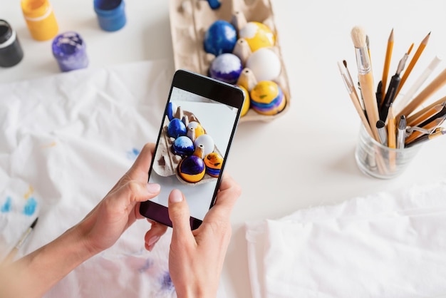 Mujer coloreando huevos de Pascua en la cocina tomando fotos en el móvil