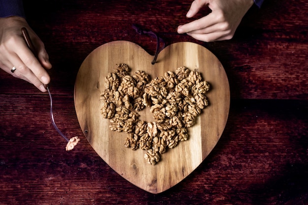 Una mujer come nueces de una bandeja de madera en forma de corazón Fondo de madera Nueces sin cáscara Alimentación saludable