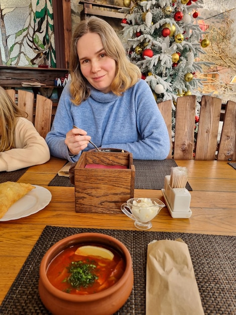 Una mujer come sopa en una mesa de café con un árbol de Navidad