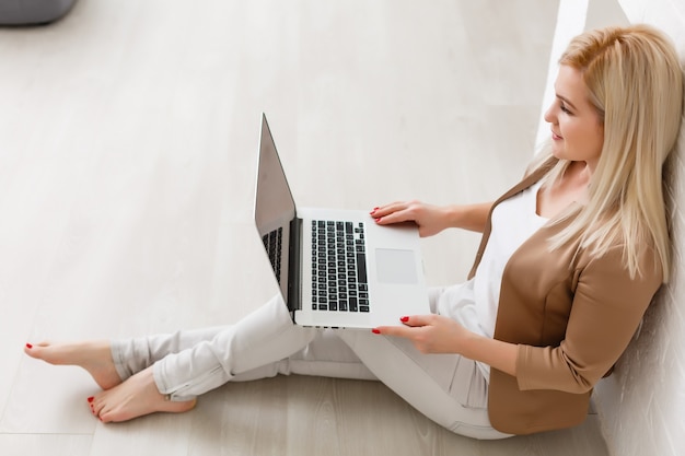 Mujer de comercio electrónico. Mujer joven con computadora para compras en línea, sentada en el suelo