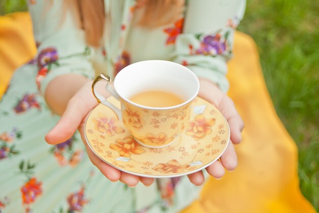 La mujer en la comida campestre se sienta en la cubierta amarilla y sostiene la taza de té.