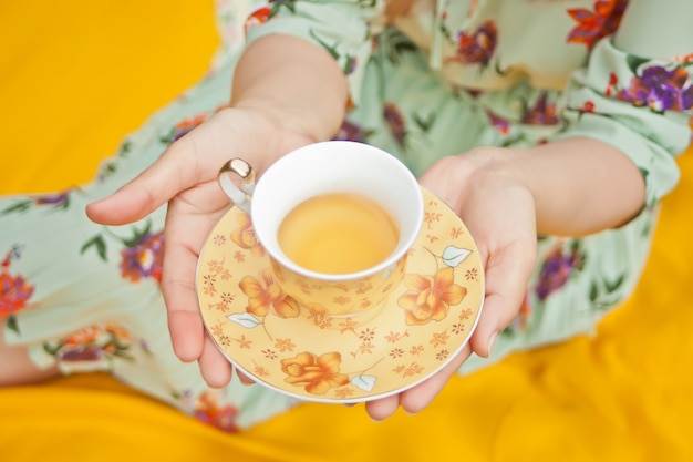 La mujer en la comida campestre se sienta en la cubierta amarilla y sostiene la taza de té.