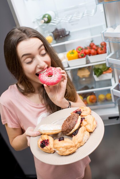 Mujer con comida dulce cerca del refrigerador