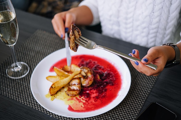 Mujer comiendo carne y bebiendo champán en un restaurante.