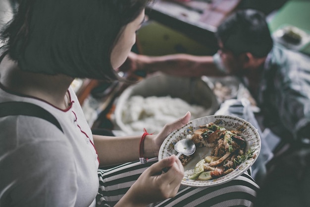 Foto mujer comiendo comida en un cuenco contra el mercado flotante