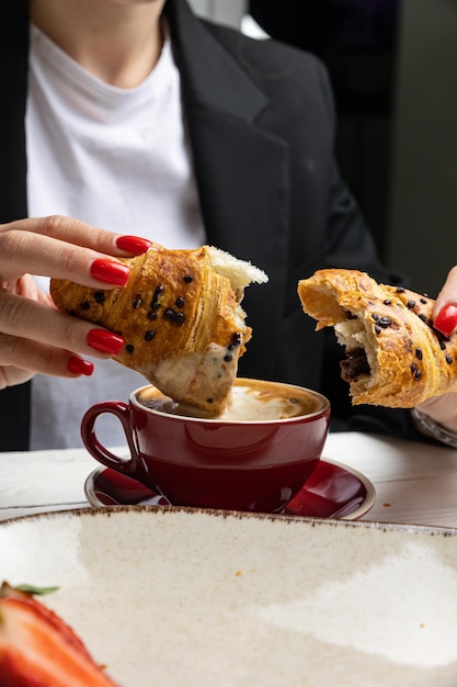 Una mujer comiendo un croissant y café.