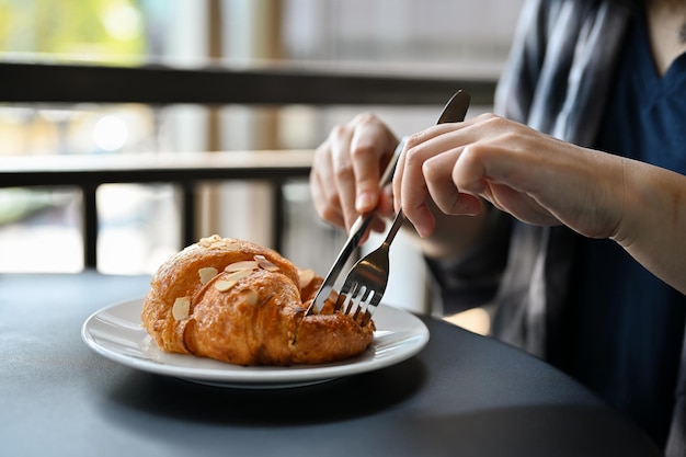 Una mujer comiendo un delicioso croissant francés recién hecho para desayunar en la cafetería