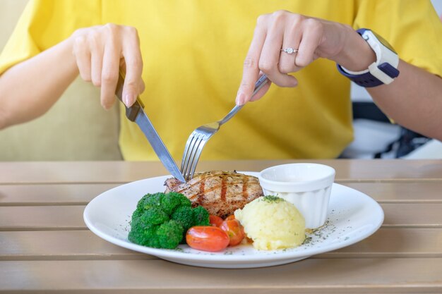 Mujer comiendo un delicioso filete de cerdo a la parrilla con tomate brócoli y puré de papa en un plato blanco