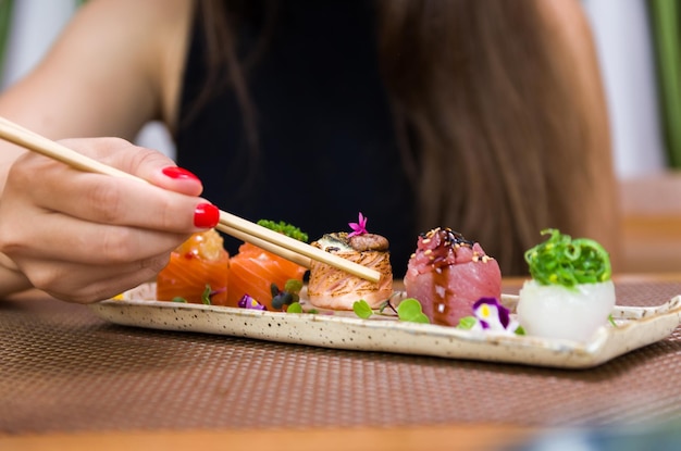 Mujer comiendo delicioso sushi gunkan closeup en palillos