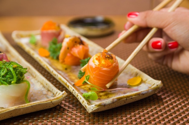 Mujer comiendo delicioso sushi gunkan closeup en palillos