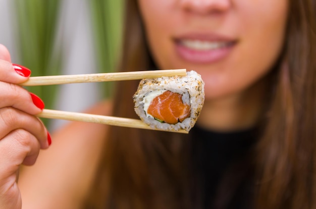 Mujer comiendo delicioso sushi gunkan closeup en palillos