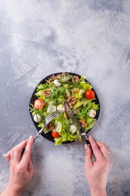 Mujer comiendo ensalada dietética con tomates queso mozzarella rúcula y nueces Concepto de comida saludable Vista superior espacio de texto