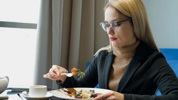 Mujer comiendo ensalada sentado en la cafetería, espacio de copia