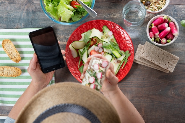 Mujer comiendo una ensalada vegana y usando un teléfono inteligente, vista superior