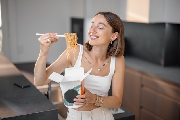 Mujer comiendo fideos de envases para llevar en casa