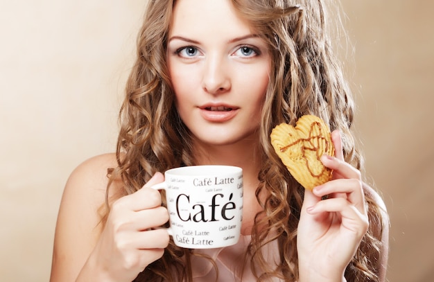 Foto mujer comiendo galletas y tomando café. modelo femenino joven hermoso adorable lindo.