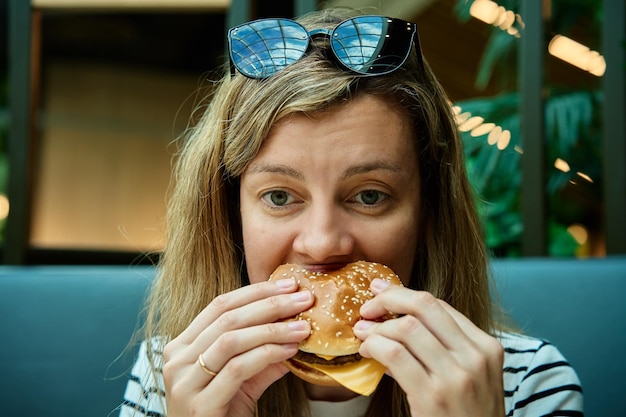 Mujer comiendo hamburguesa en un restaurante Toma de cerca una mujer mordiendo una hamburguesa mujer hambrienta