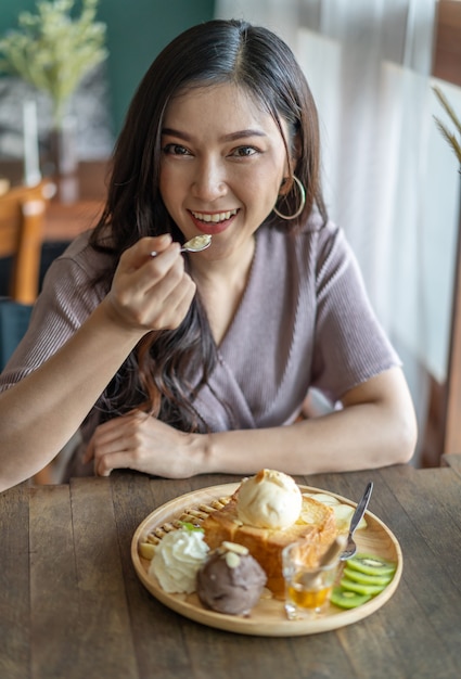 Mujer comiendo pan tostado de miel, postre dulce en café