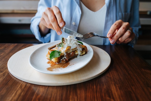 Mujer comiendo un pastel cubierto con helado con tenedor y cuchillo sin rostro