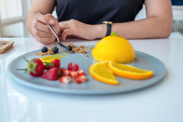 Una mujer comiendo pastel de naranja con una mezcla de frutas con una cuchara en el café