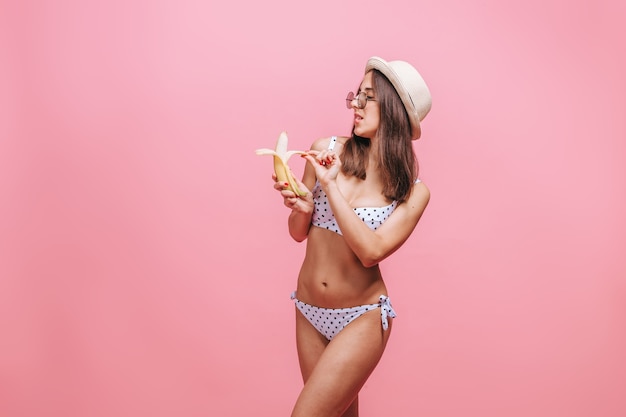 mujer comiendo un plátano en una pared rosa