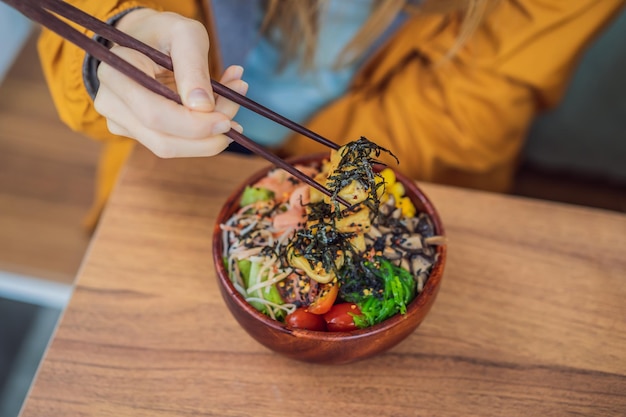 Mujer comiendo poke bowl orgánico crudo con arroz y verduras en primer plano en la mesa vista desde arriba