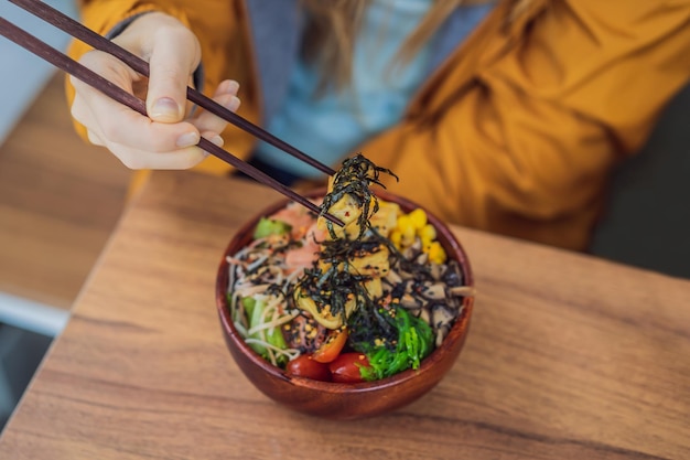 Mujer comiendo poke bowl orgánico crudo con arroz y verduras en primer plano en la mesa vista desde arriba