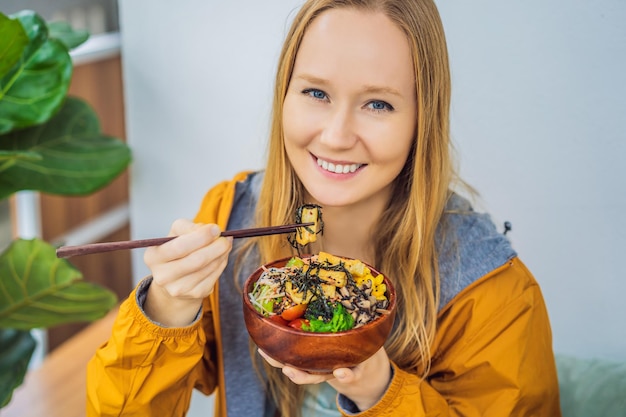Mujer comiendo poke bowl orgánico crudo con arroz y verduras en primer plano en la mesa vista desde arriba