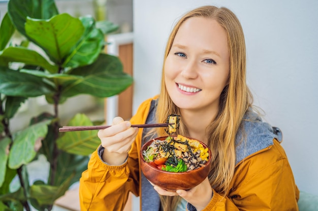 Mujer comiendo poke bowl orgánico crudo con arroz y verduras en primer plano en la mesa vista desde arriba