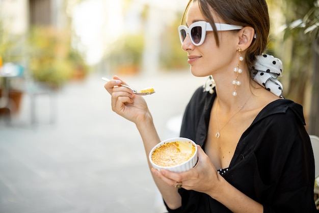 Mujer comiendo postre con creme brulee en el restaurante al aire libre