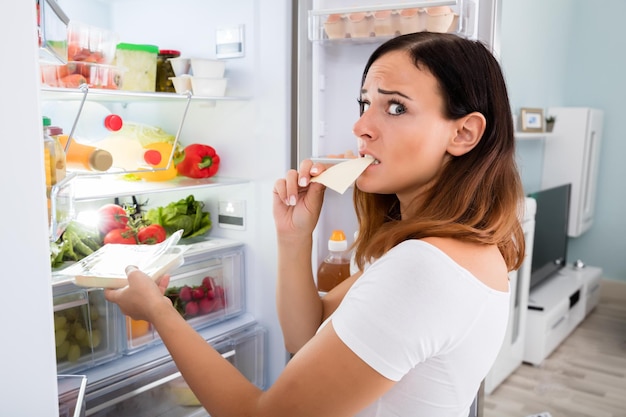 Mujer comiendo queso delante del frigorífico