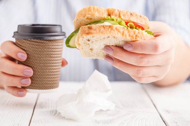 Mujer comiendo un sándwich de desayuno y tomando café mientras trabaja