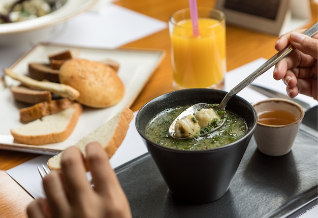 Mujer comiendo sopa verde con salsa en un tazón negro