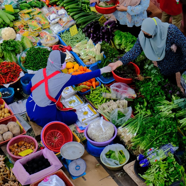 Una mujer compra verduras en un mercado con una bolsa azul a la izquierda.