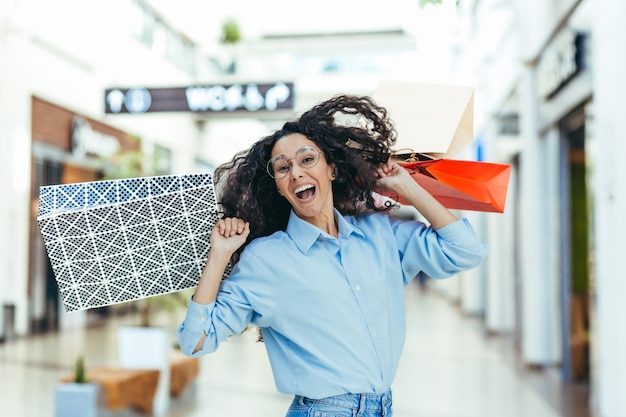 Mujer compradora feliz mirando a la cámara y mujer hispana sonriente con el pelo rizado bailando y saltando