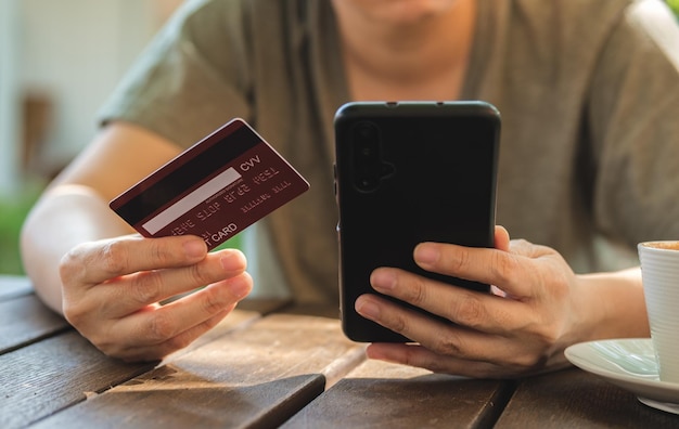 Foto mujer comprando en línea con tarjeta de crédito en una cafetería al aire librecerca de la mano que sostiene el teléfono inteligente