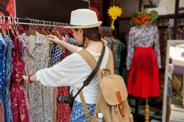 mujer comprando en el mercado de fin de semana de Chatuchak en las vacaciones de Tailandia eligiendo vestidos coloridos comprando en la tienda de la calle para ella y sus amigos y familiares como regalos.