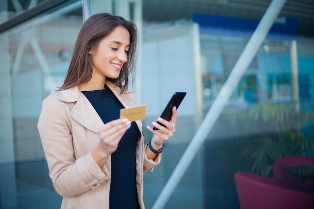 Mujer de compras con tarjeta de crédito Hermosa joven con tarjeta dorada usando el teléfono